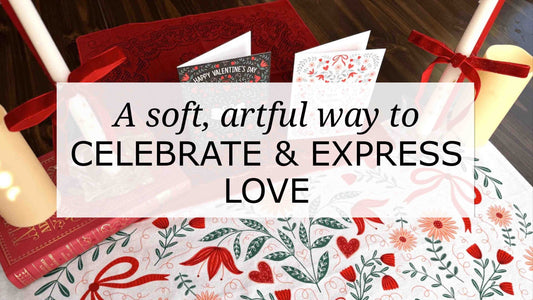 Valentine’s tabletop scene styled with a folk-art Sweetheart table runner, illustrated love cards, red candles tied with ribbon, and books, featuring text overlay celebrating love in a soft, artful way.