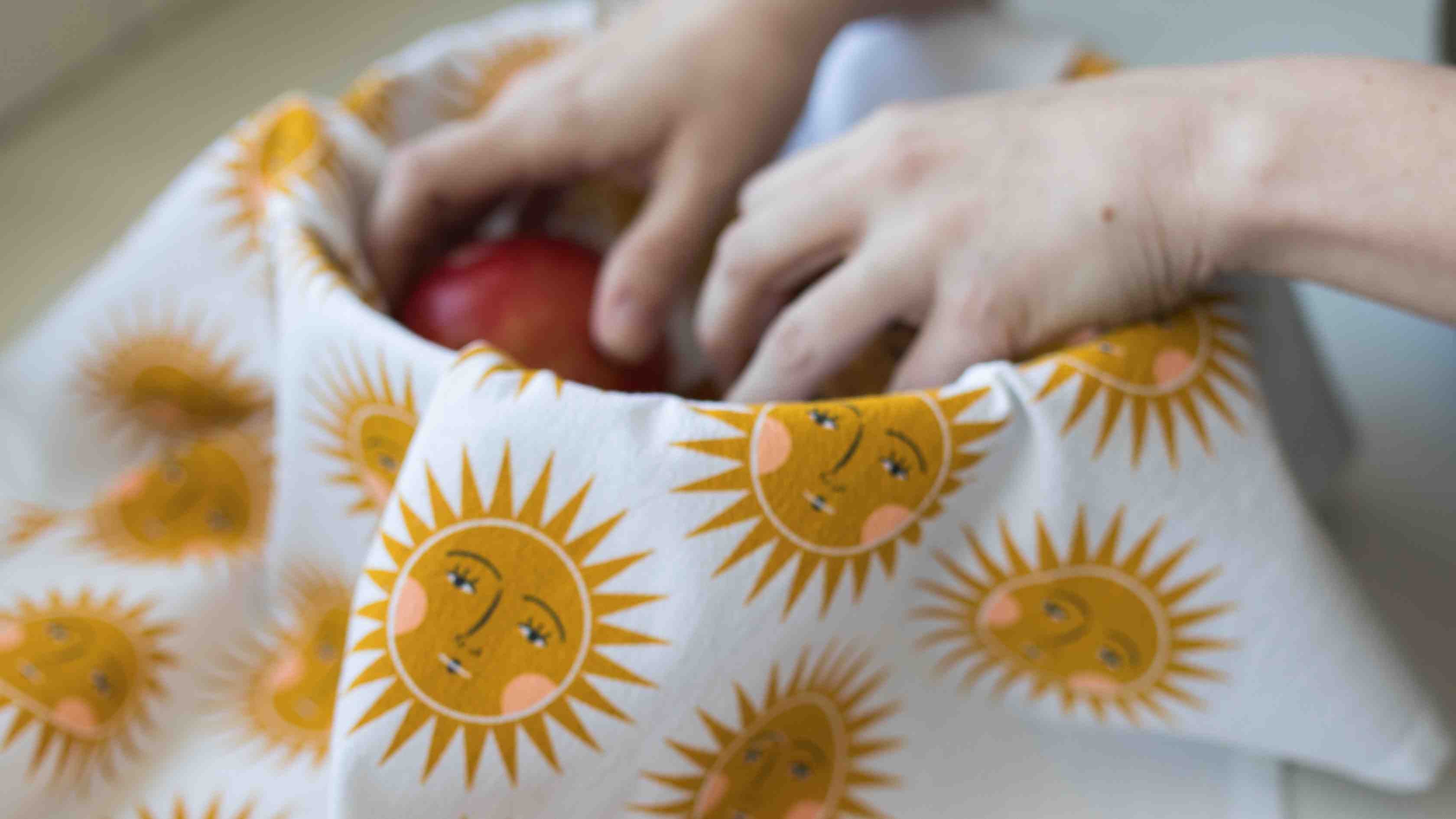 Sun Tea Towel featuring whimsical golden sun faces used to hold fresh fruit, demonstrating a creative table setting alternative to traditional napkins.