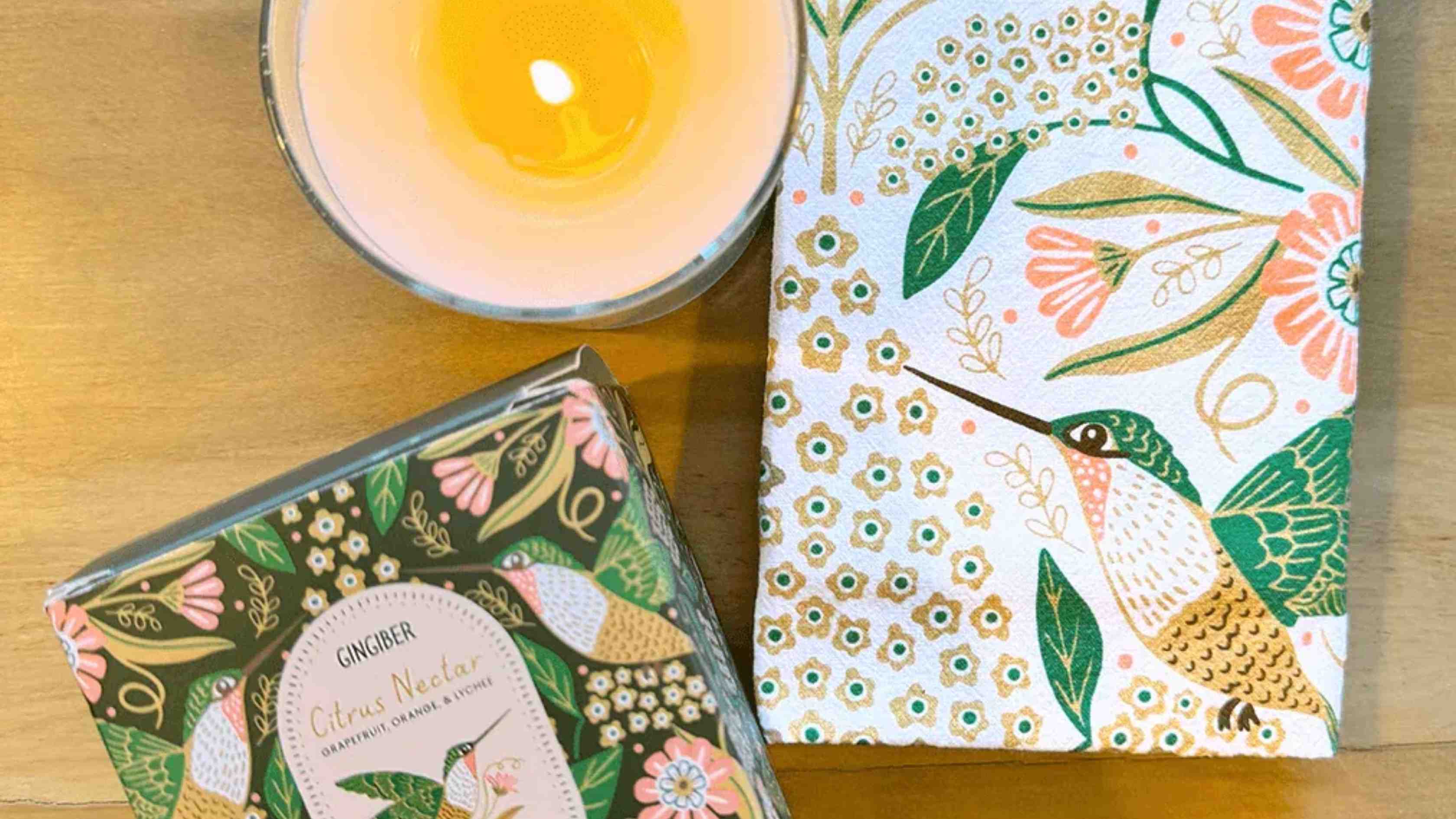 Hummingbird Candle & Tea Towel Bundle featuring a floral hummingbird tea towel paired with a Citrus Nectar scented candle on a gold surface.