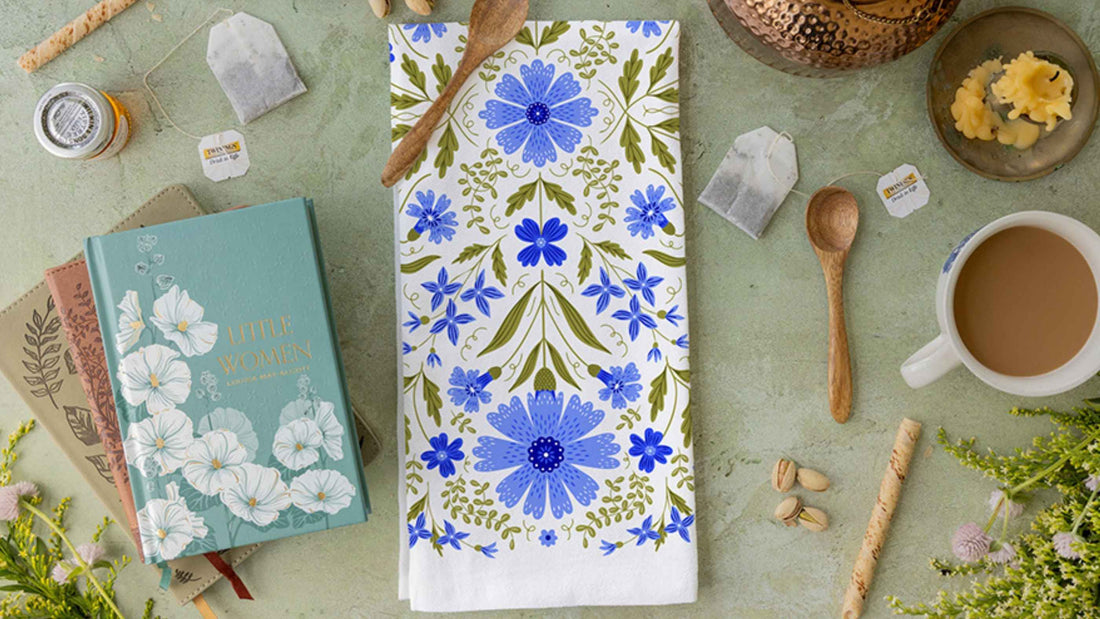 Tea Towel Club design featuring intricate blue floral and botanical illustrations, styled with books, tea bags, a warm cup of tea, wooden spoons, and fresh flowers.