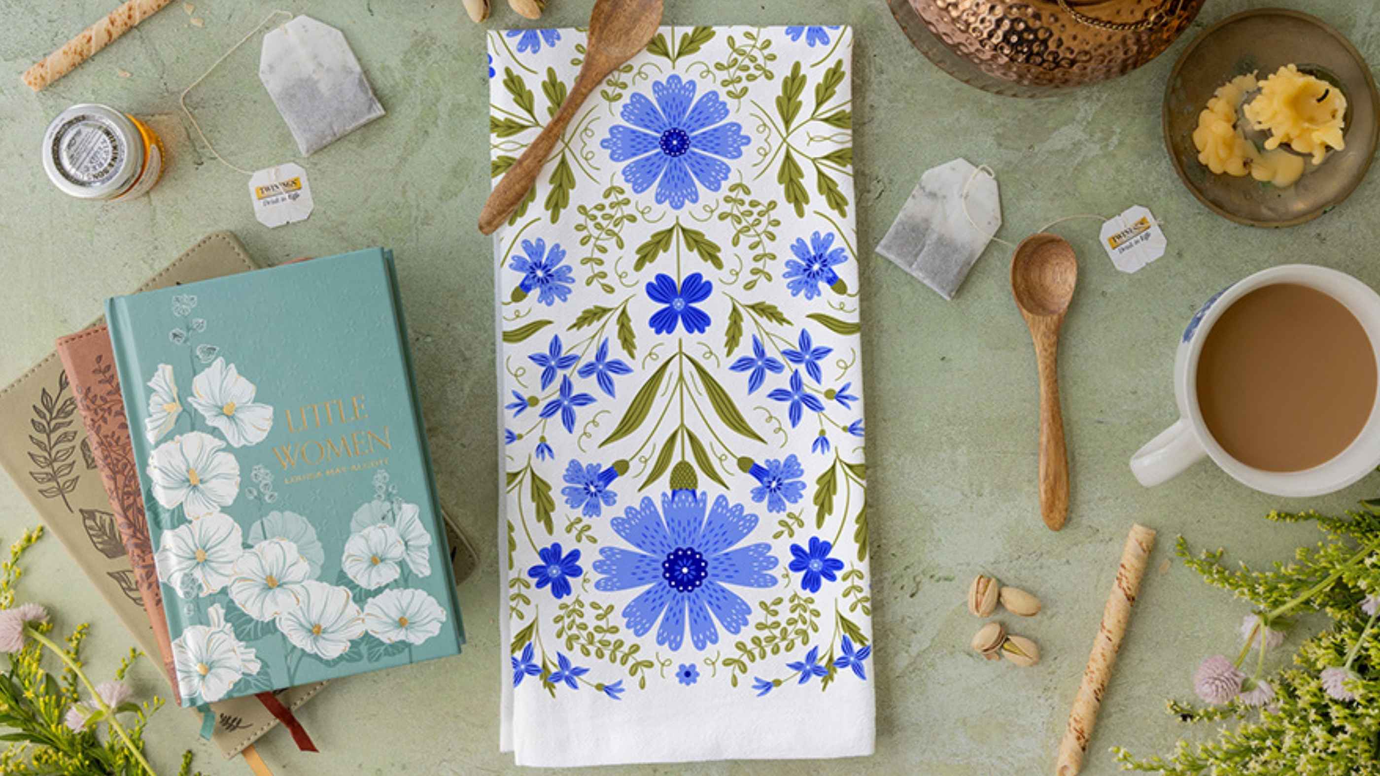 Tea Towel Club design featuring intricate blue floral and botanical illustrations, styled with books, tea bags, a warm cup of tea, wooden spoons, and fresh flowers.