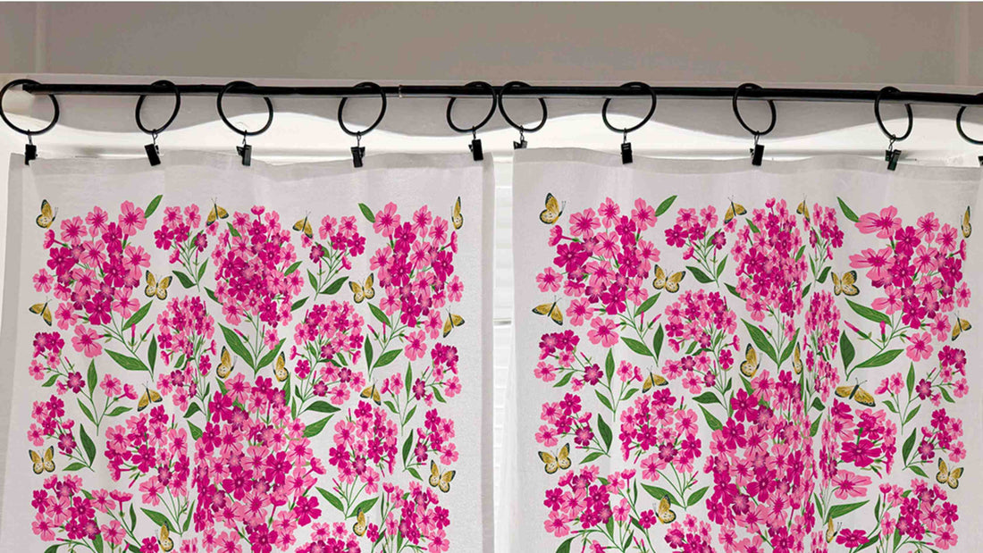 Pink Perennial Café Curtains hanging from black curtain rings, featuring vibrant pink perennial flowers, green foliage, and delicate butterflies.