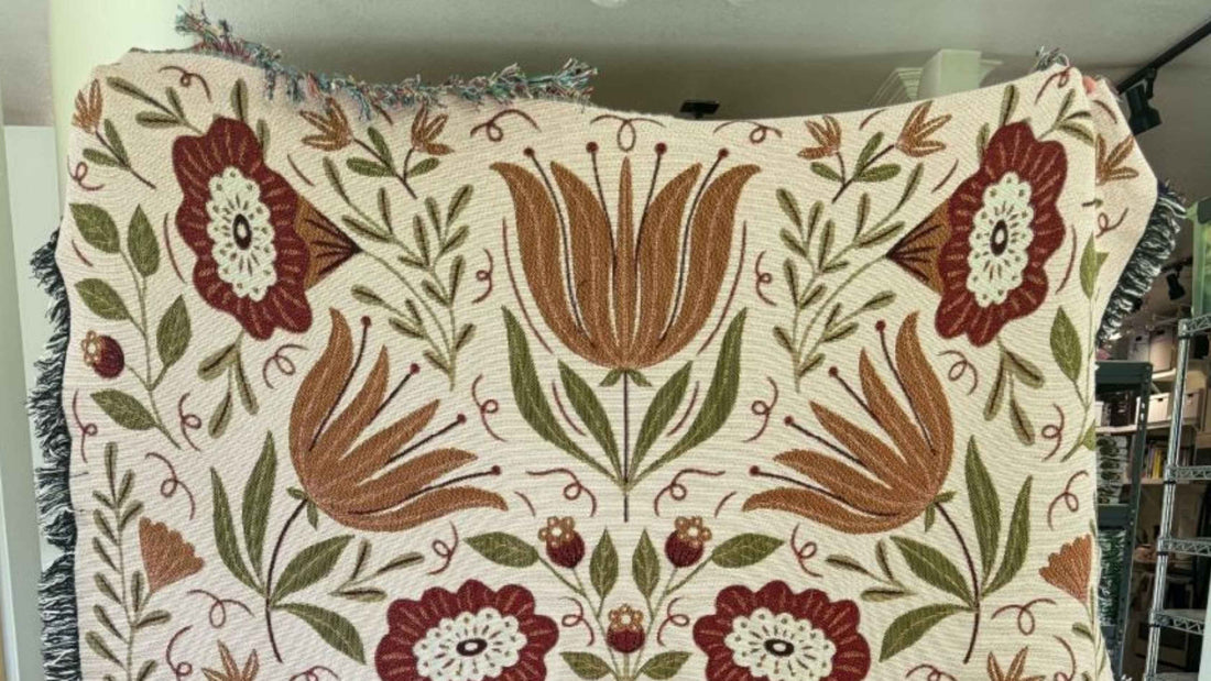 Folk Floral Blanket featuring warm rust, burgundy, and olive green botanical designs on a cream background, with a cozy woven texture and fringed edges, perfect for adding warmth to a coffee lover’s favorite reading or sipping spot.
