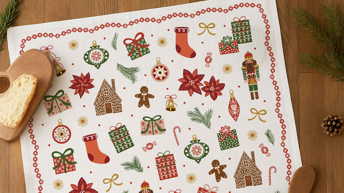 Christmas Tree Tea Towel featuring colorful holiday illustrations of wrapped gifts, ornaments, stockings, gingerbread houses, nutcrackers, poinsettias, and candy canes, styled on a wooden table for a festive white elephant gift idea.