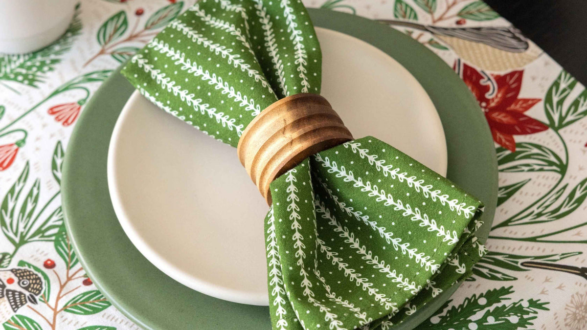 Poinsettia & Pine Runner featuring festive red and green botanical illustrations, styled with green dinnerware and a patterned cloth napkin for a warm and inviting Thanksgiving table setting.