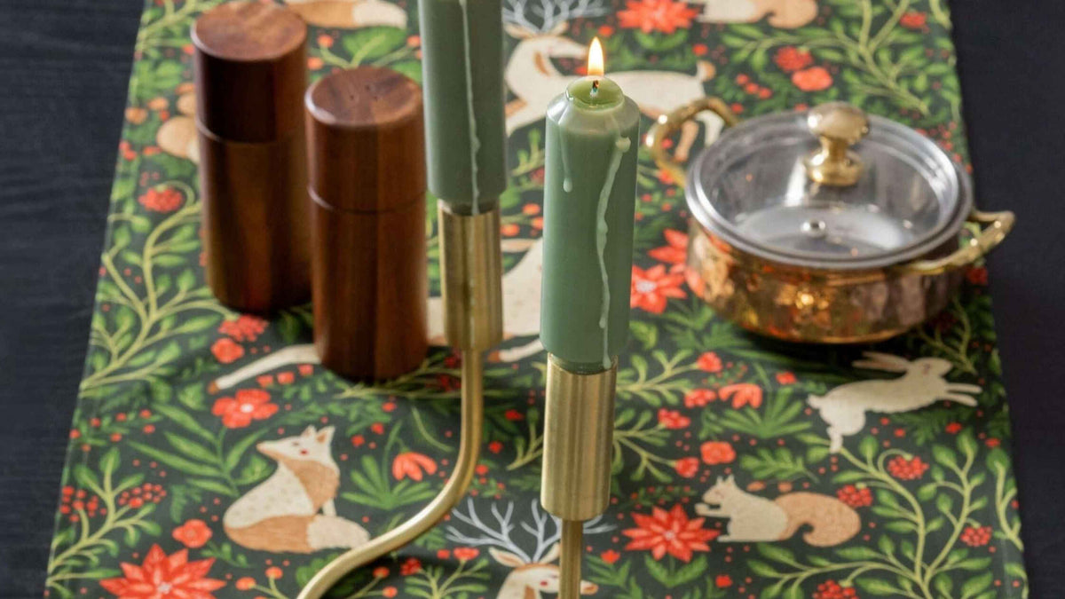 Evergreen Christmas Forest Table Runner featuring woodland animals, greenery, and red florals, styled with green taper candles and festive tabletop accents.