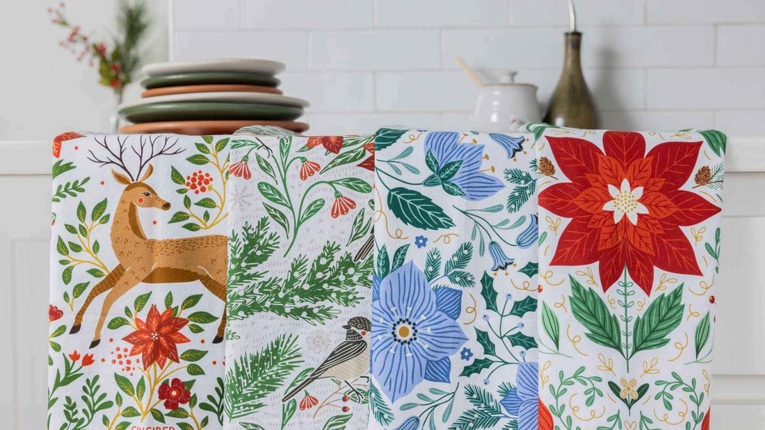 Holiday Best Sellers Tea Towel Bundle featuring festive deer, winter birds, blue florals, greenery, and poinsettia designs displayed in a bright kitchen.