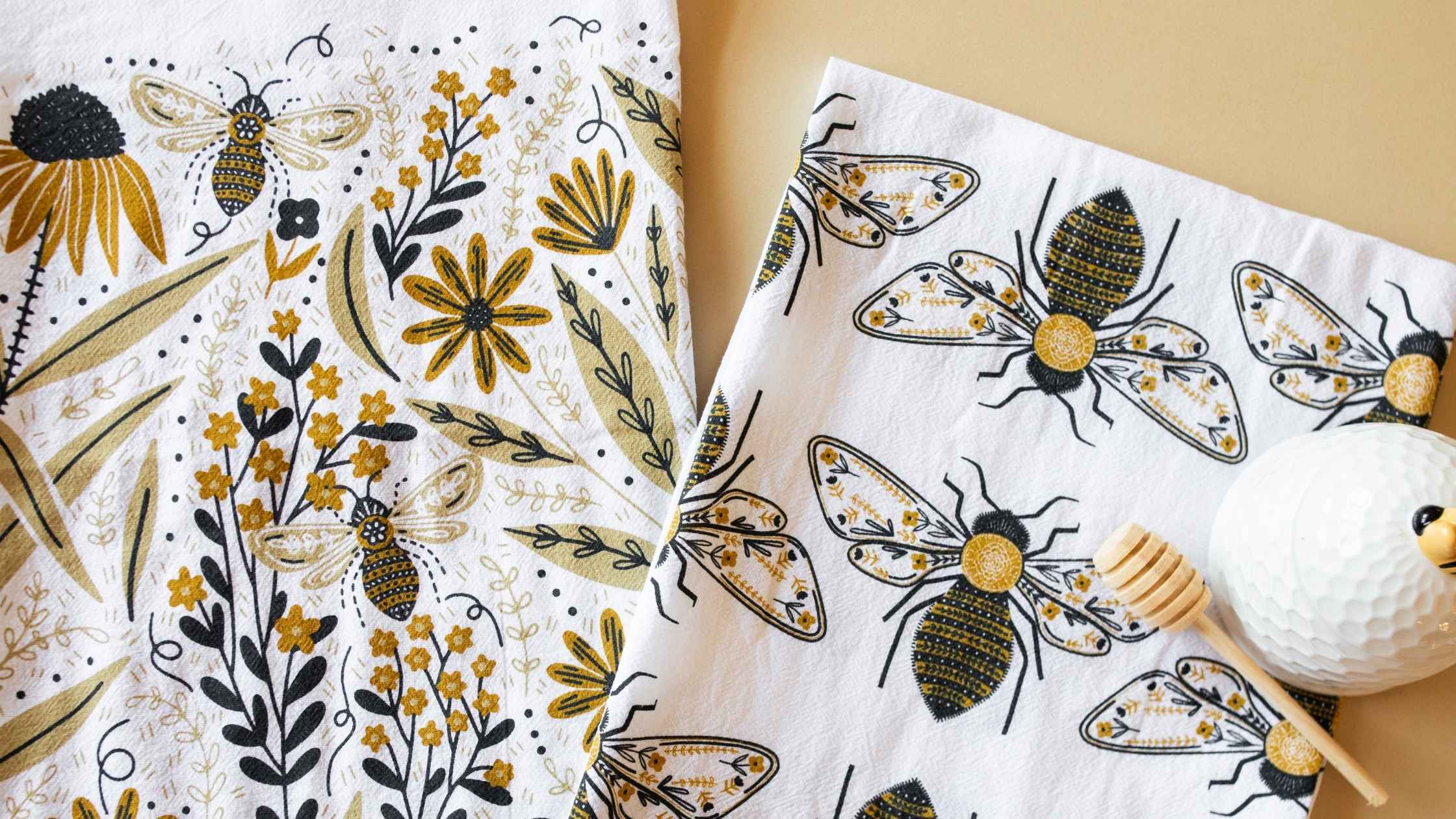 A Bee Garden Tea Towel Bundle displayed side by side, featuring hand illustrated bees, wildflowers, and botanical details in warm golden, black, and cream tones.