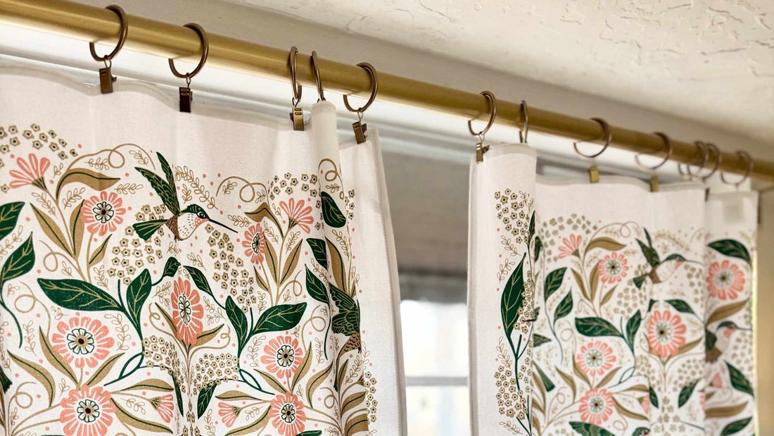 Hummingbird Café Curtains featuring hand illustrated hummingbirds, delicate flowers, and leafy botanical details hanging from a brass café curtain rod.