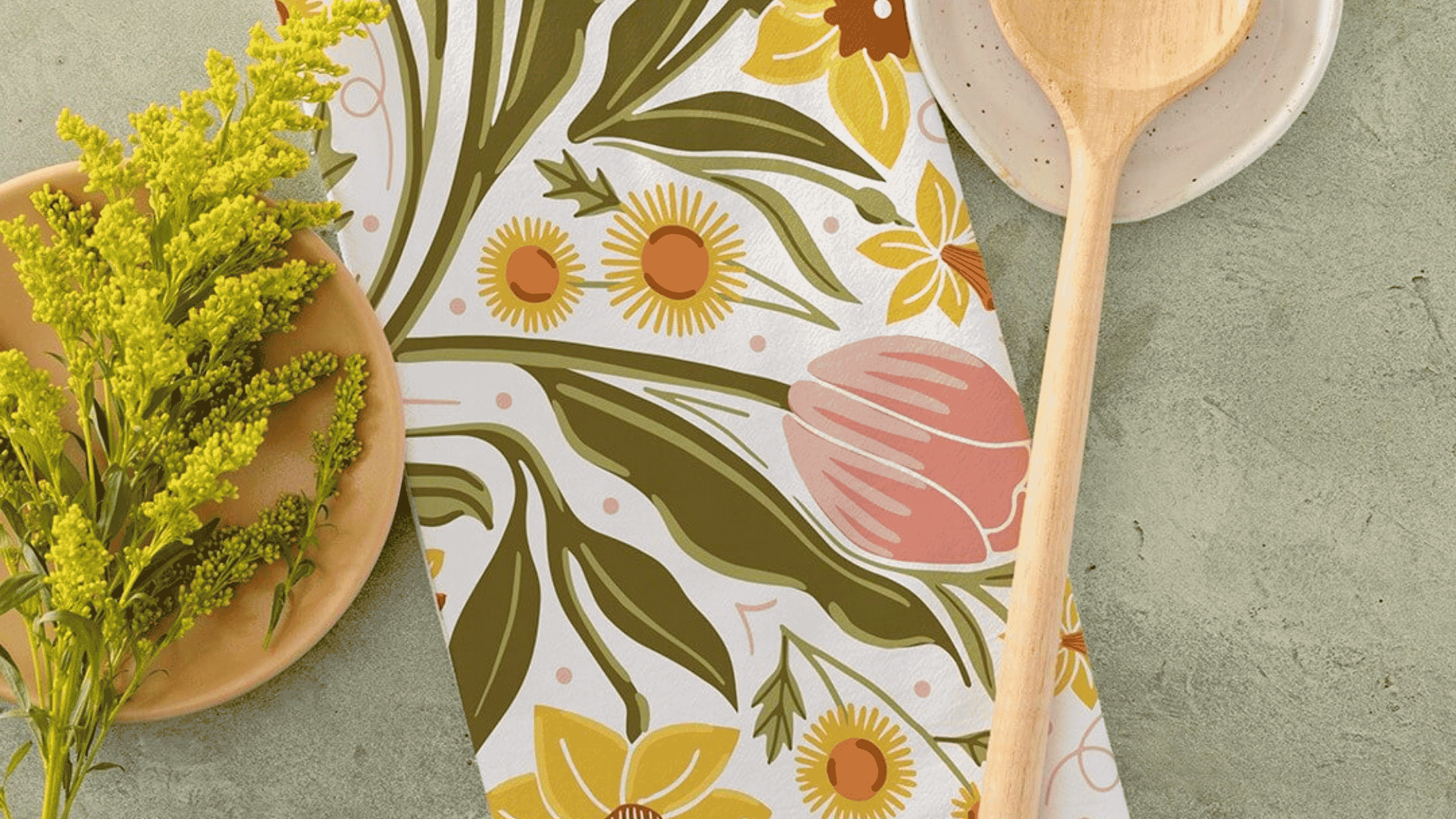 A Daffodil Dreams Tea Towel featuring hand illustrated daffodils, tulips, and leafy botanical details in soft yellow, blush pink, and green tones.