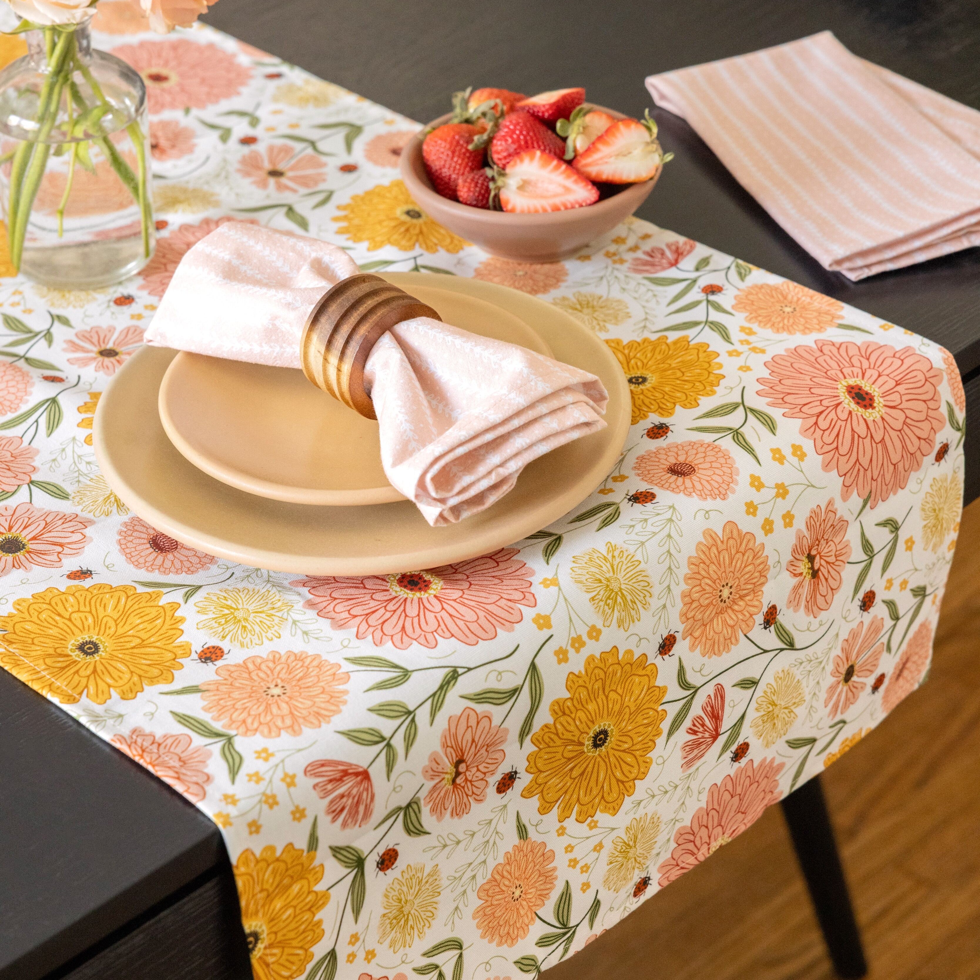 Floral tablecloth with plates, napkins, and a bowl of strawberries on a dining table.