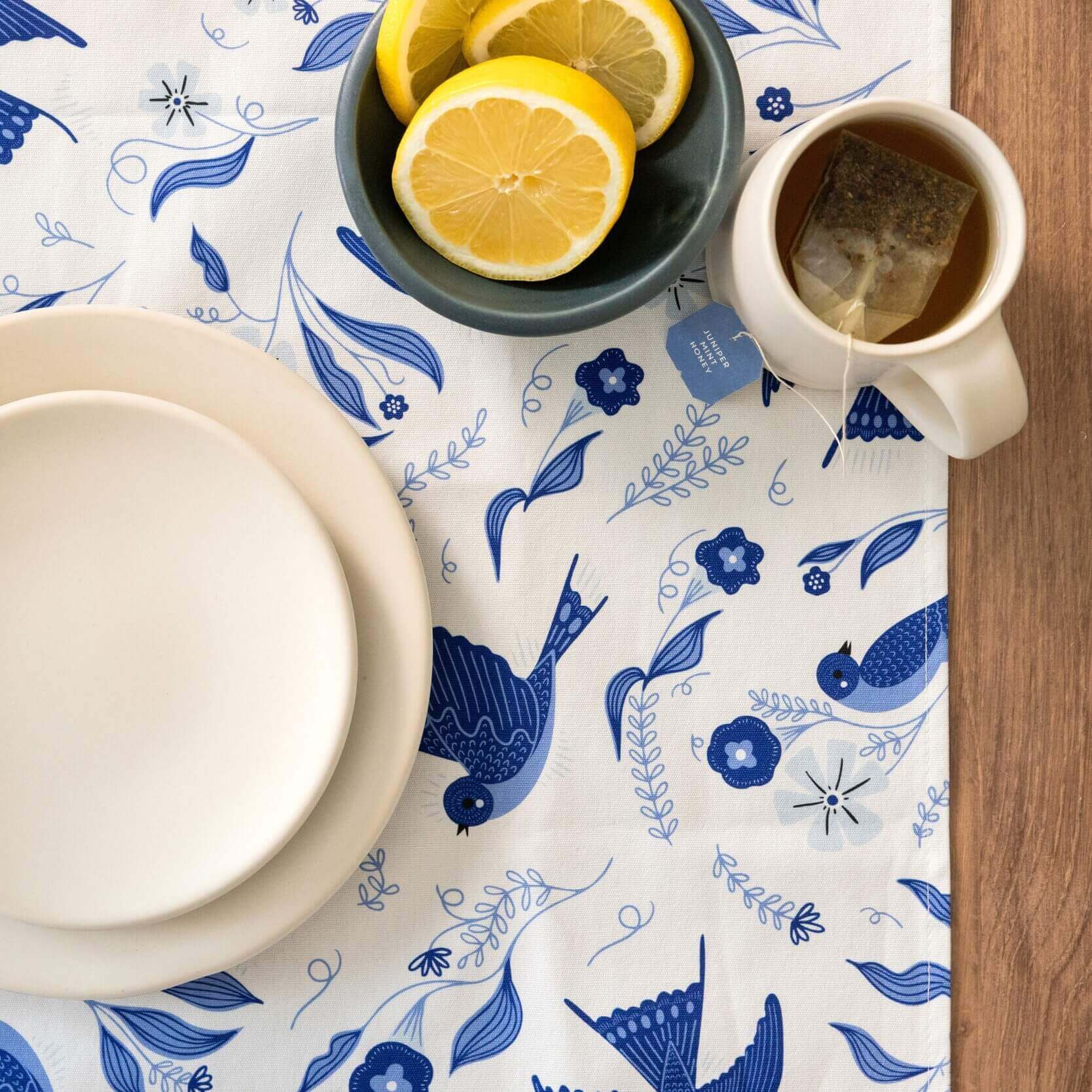 Table setting with a blue and white patterned tablecloth, lemon slices, and a teacup.
