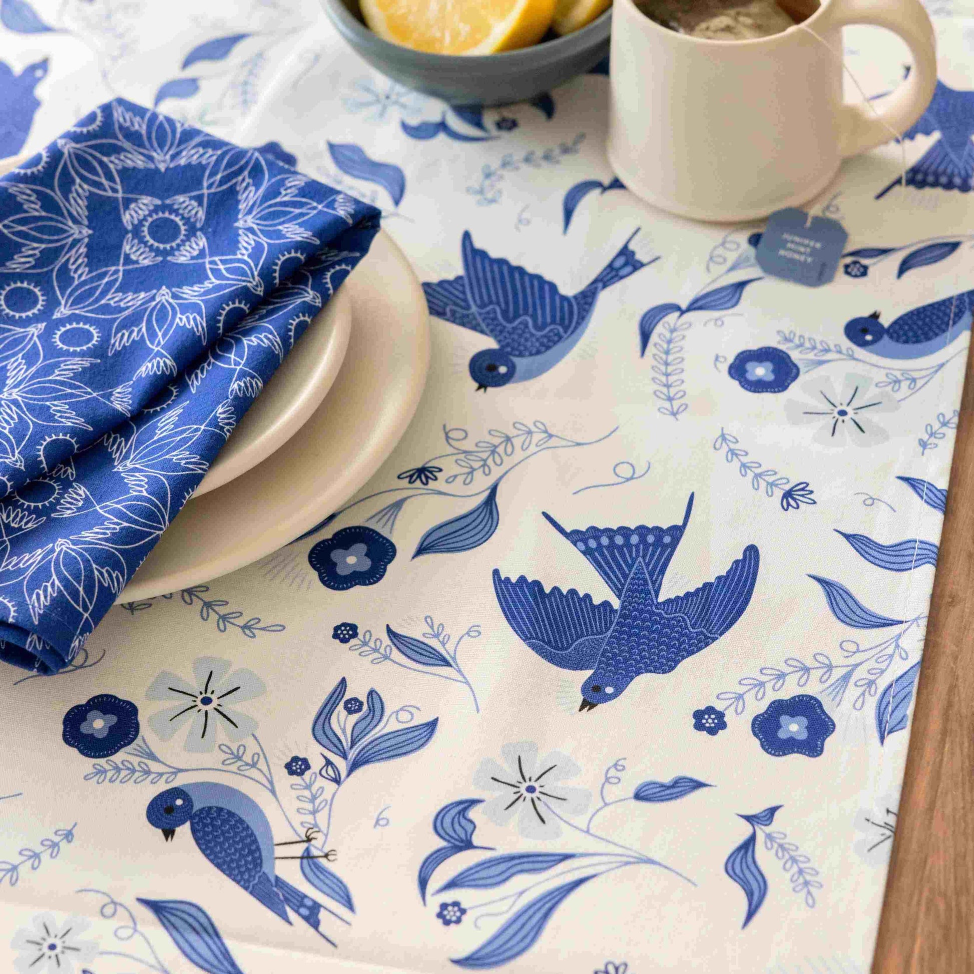 Tablecloth with blue bird and floral pattern on a table with a cup, plate, and lemon.