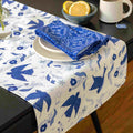 Table setting with a blue and white tablecloth featuring bird patterns, a folded blue napkin, and a bowl of lemons.