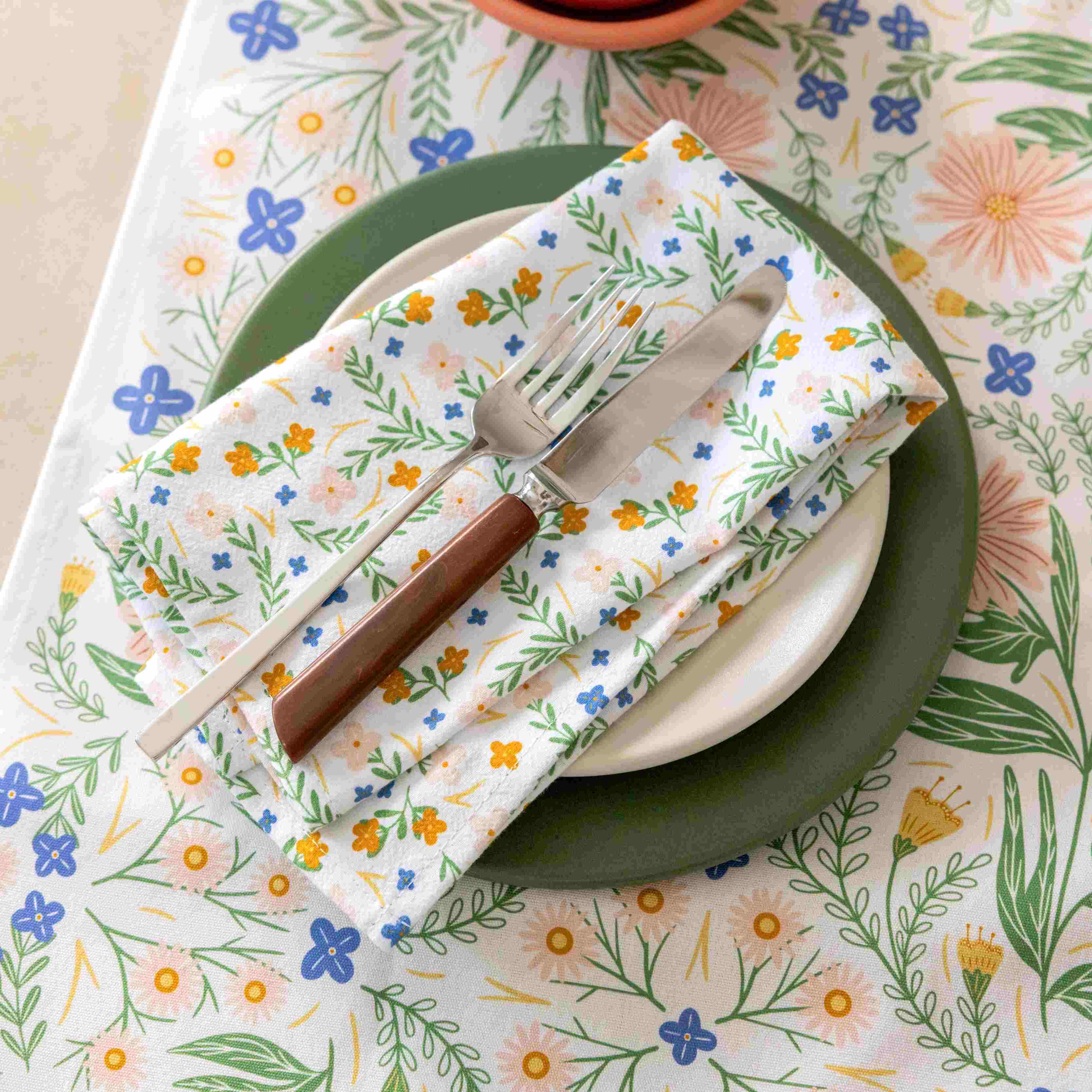 Floral-patterned napkin with cutlery on a matching plate on a floral tablecloth.