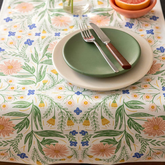 Table setting with green plates, silverware, and a floral-patterned tablecloth.