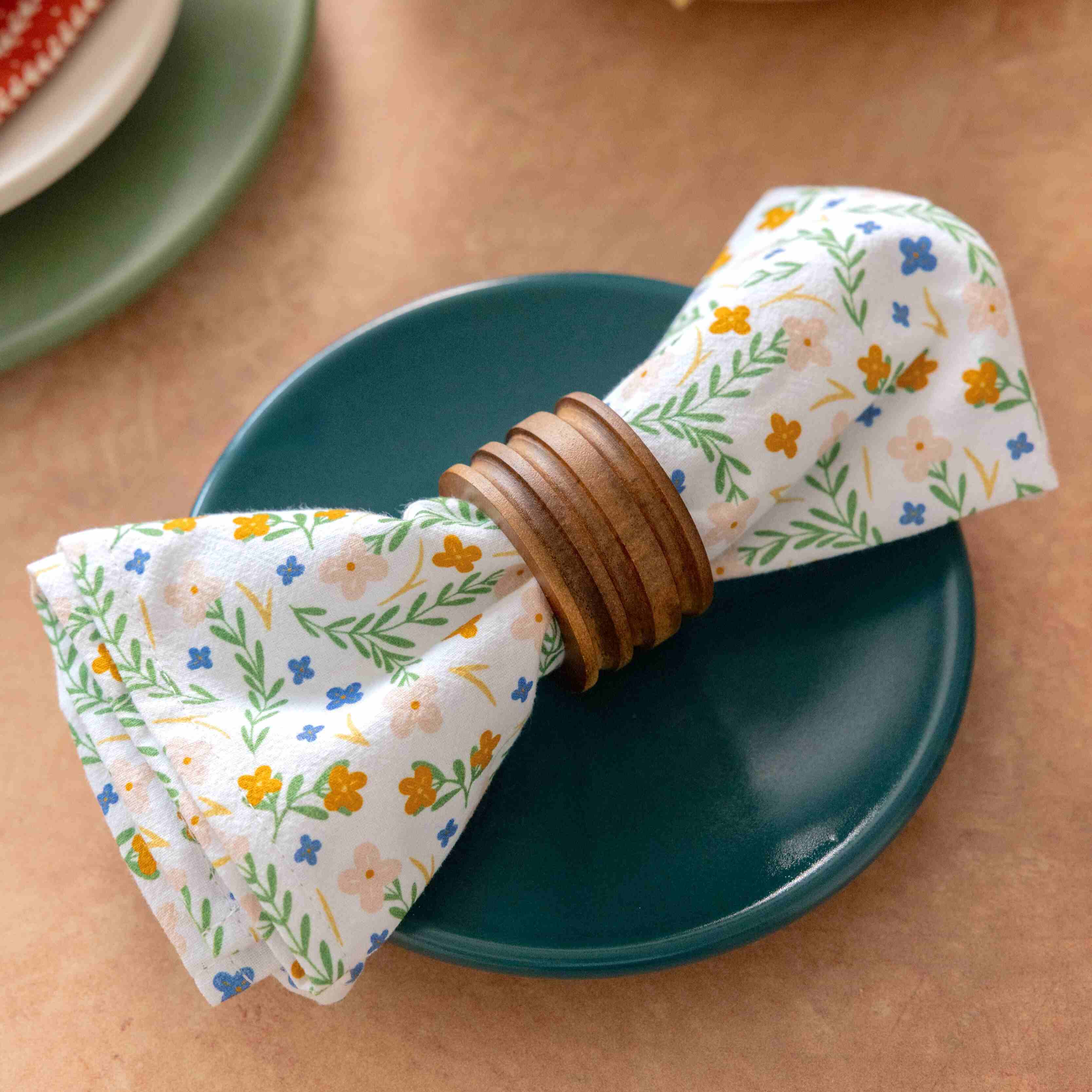 Floral-patterned napkin with wooden napkin ring on a teal plate on a beige surface