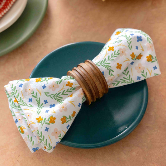 Floral-patterned napkin with wooden napkin ring on a teal plate on a beige surface