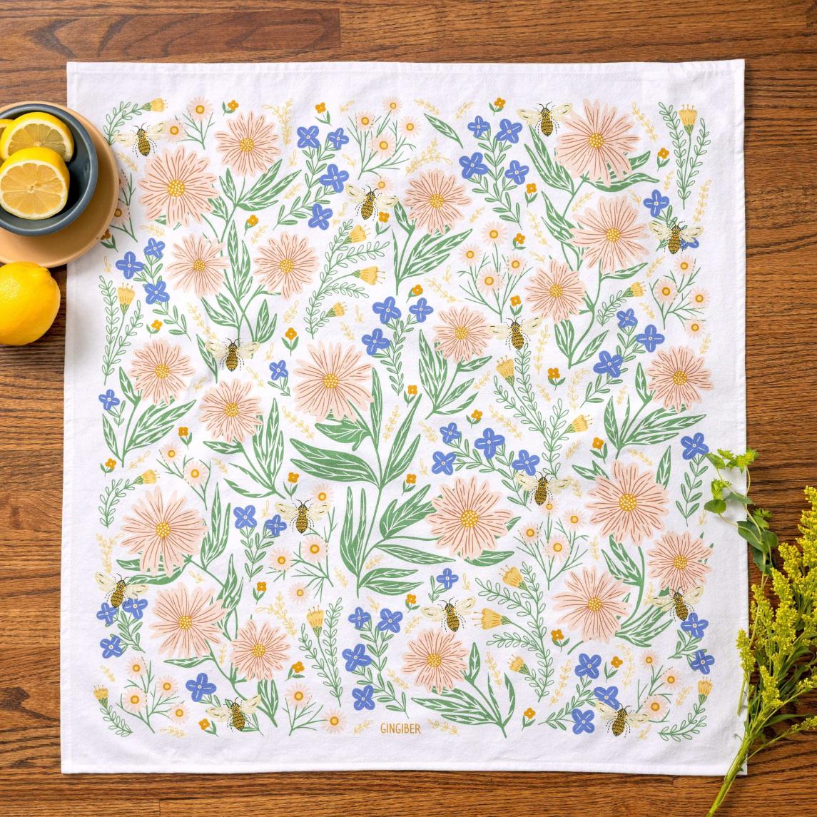 Floral patterned towel on a wooden surface with lemons and a bowl.