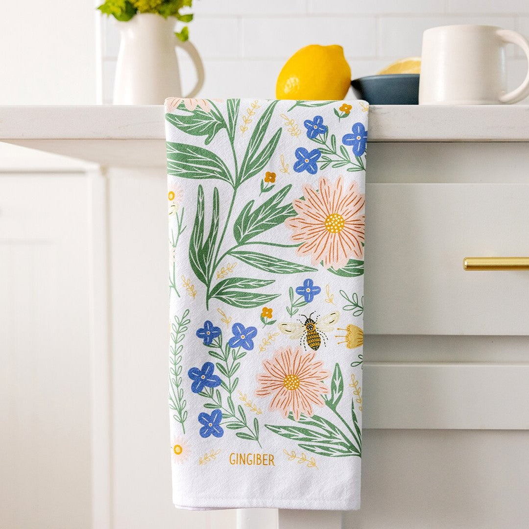 Floral patterned towel hanging on a kitchen cabinet handle with a lemon and mug in the background.