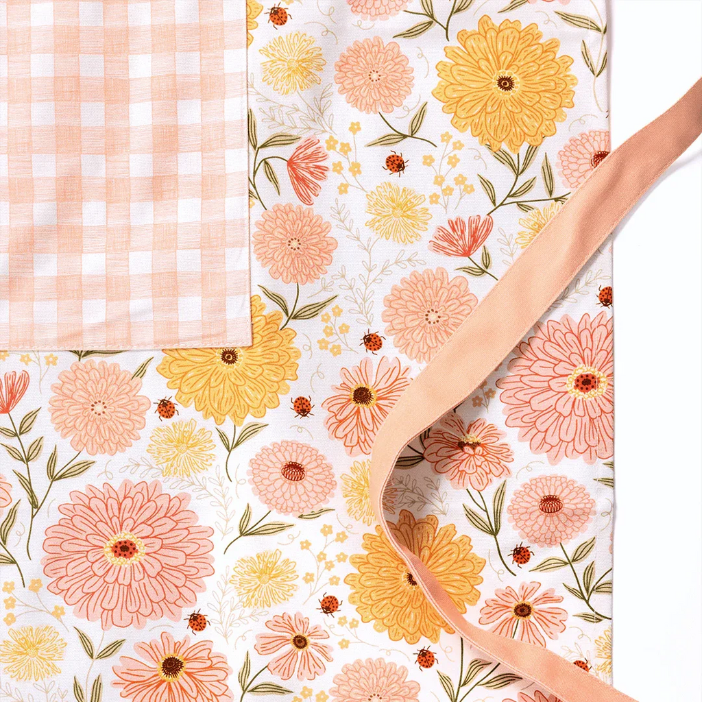 Zinnia Apron product image showcasing floral print and gingiber design with soft peach piping and tied waist, 100% cotton canvas
