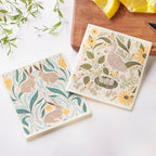 Two decorative dish cloths with animal and floral patterns on a white surface.