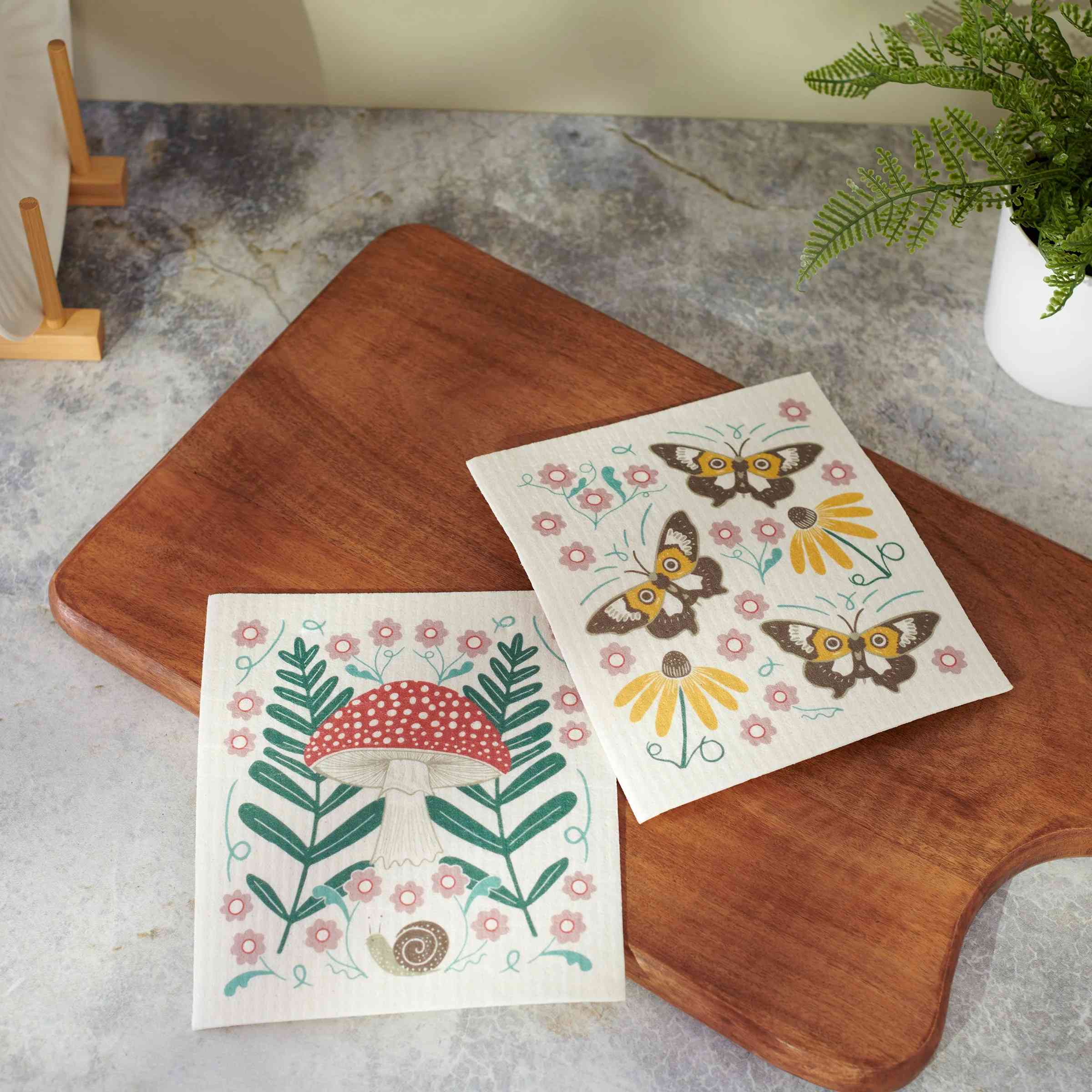 Two decorative paper sheets with nature-themed designs on a wooden surface.