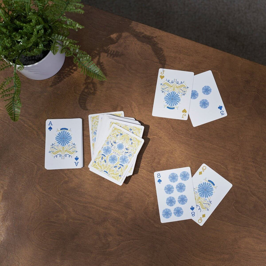 Playing cards with floral designs on a wooden table next to a potted plant.
