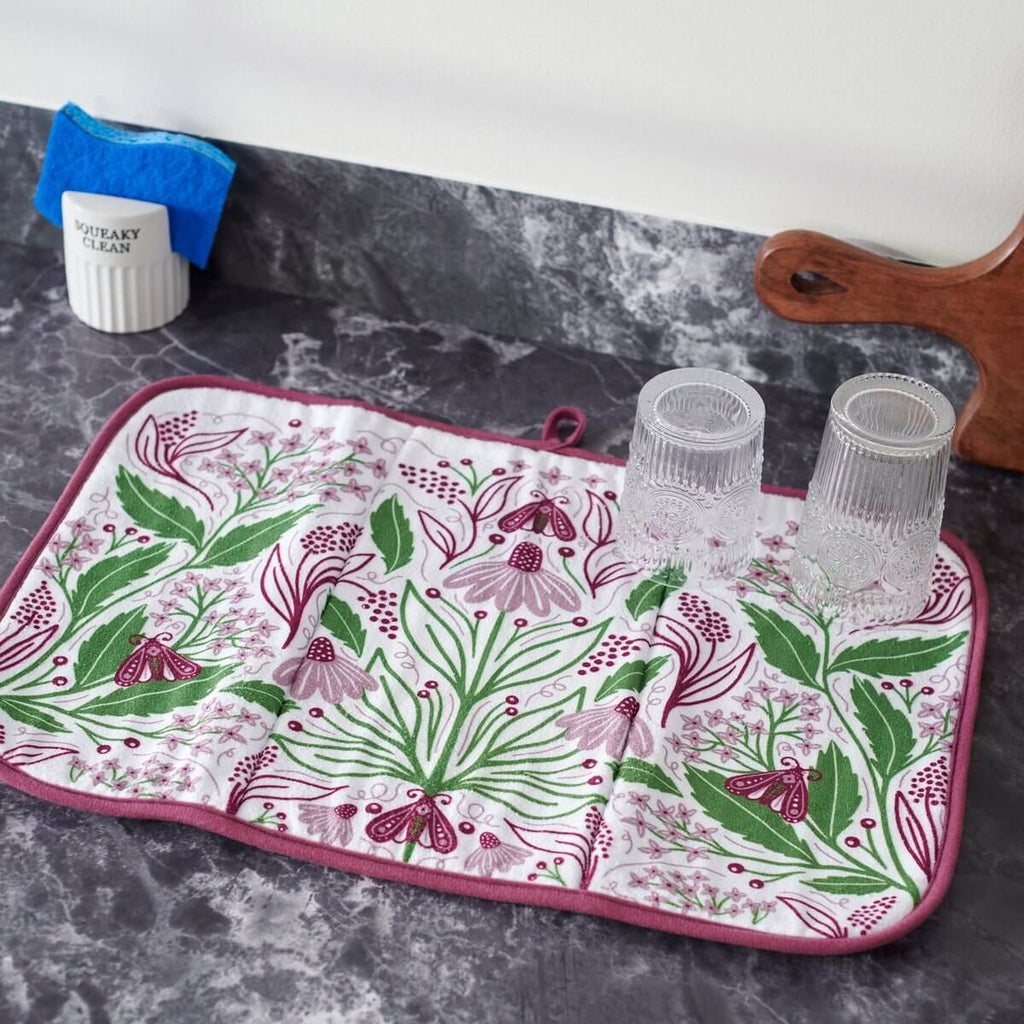Floral-patterned mat on a dark surface with cups and a towel.