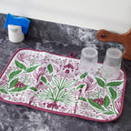 Floral-patterned mat on a dark surface with cups and a towel.