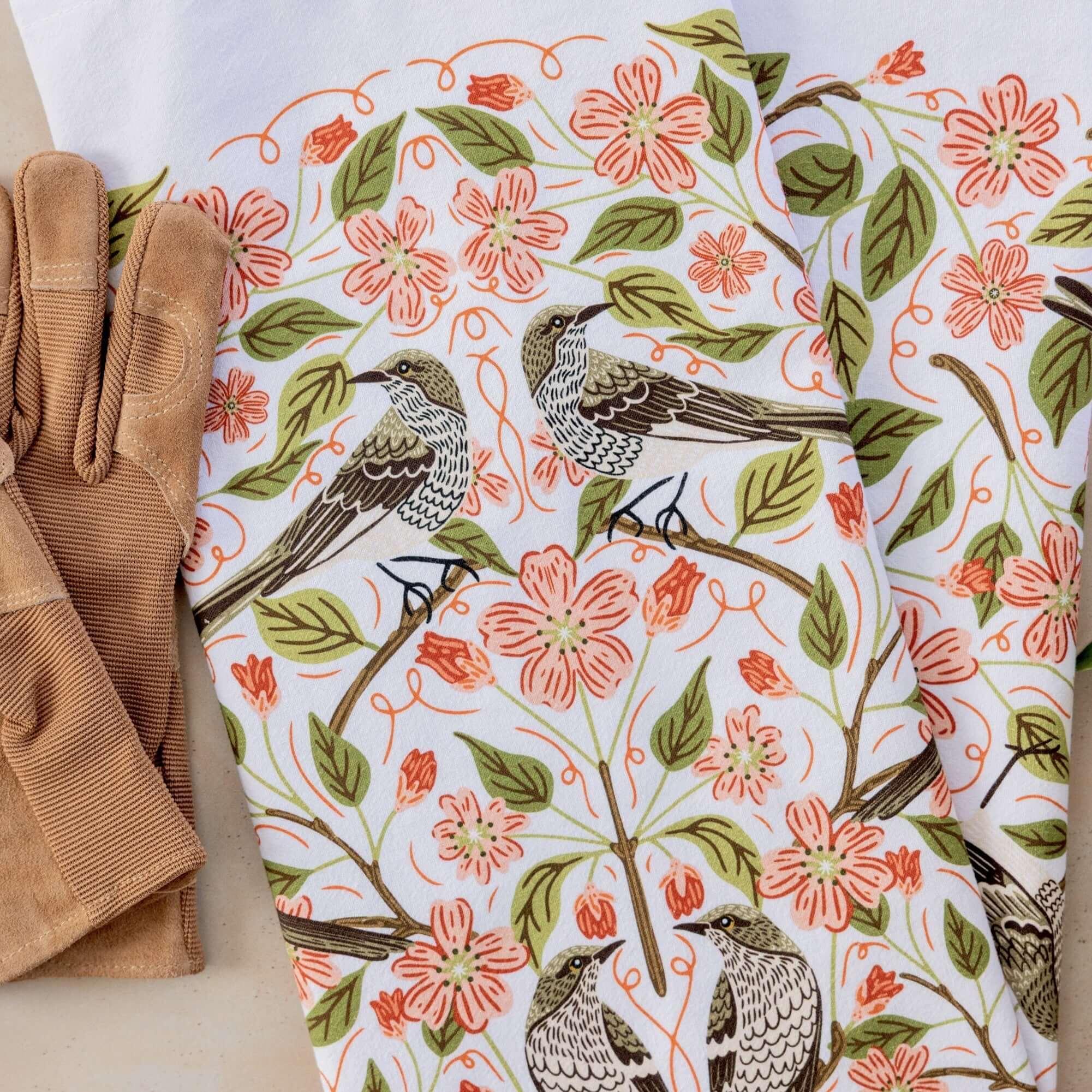 Floral and bird patterned fabric with brown gloves on a white background