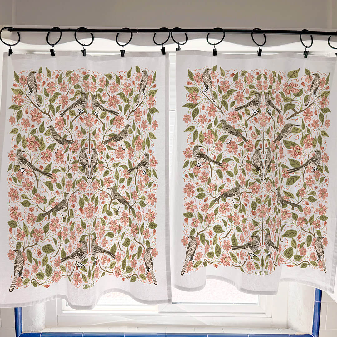 Floral and bird patterned curtains hanging on a rod.