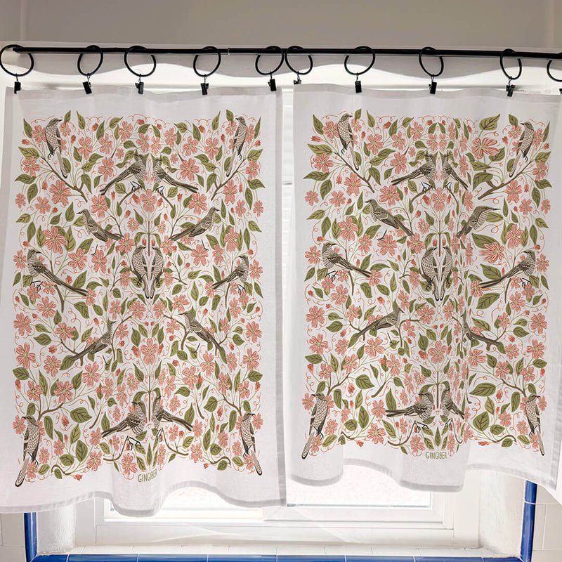 Floral and bird patterned curtains hanging on a rod.