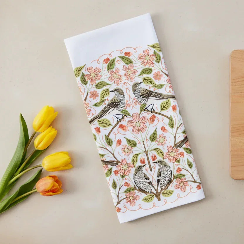 Floral and bird patterned towel with yellow tulips on a beige surface