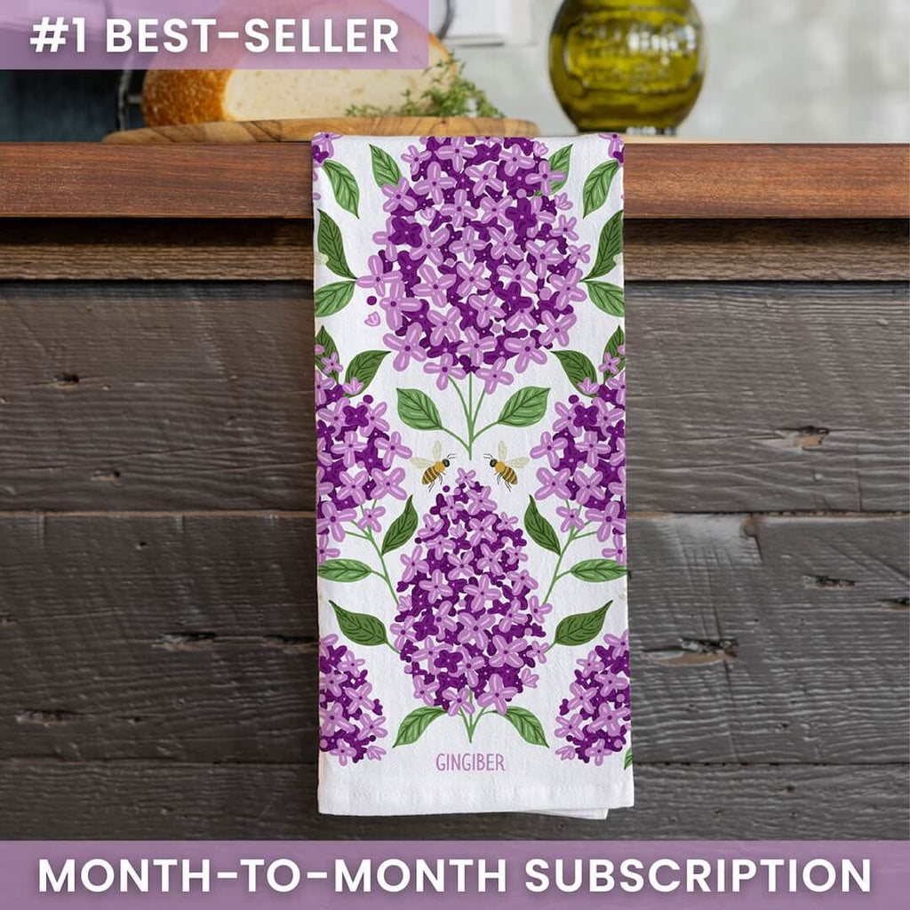Towel with purple floral design on a wooden surface, featuring the brand 'Gingiber'.