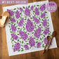 Floral towel with purple flowers on a wooden surface, featuring a price tag.