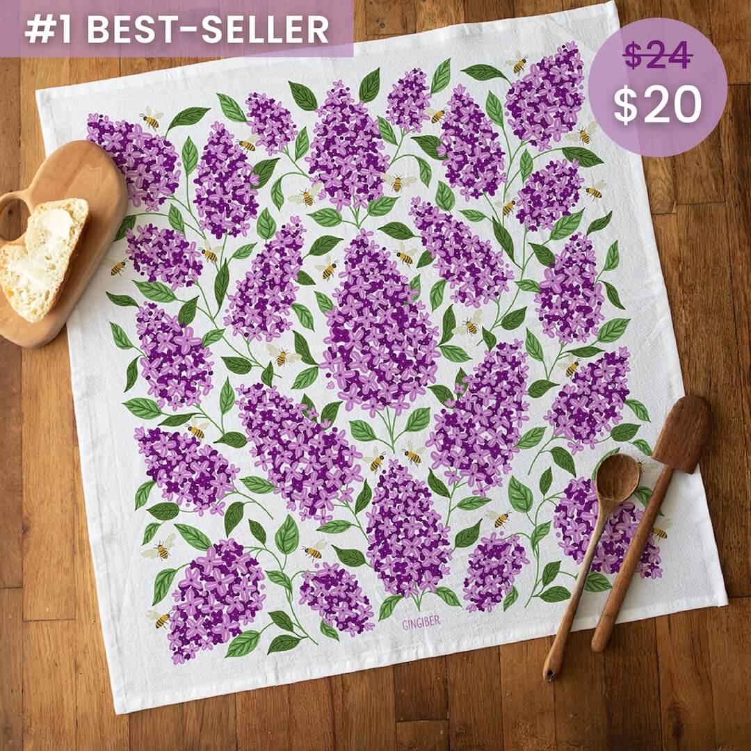 Floral towel with purple flowers on a wooden surface, featuring a price tag.