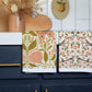 Two patterned towels on a kitchen cabinet with decorative elements in the background.