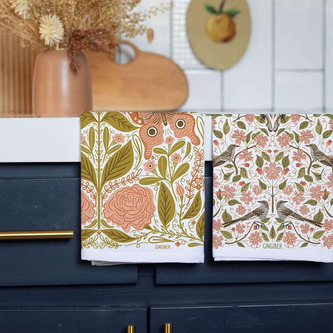 Two patterned towels on a kitchen cabinet with decorative elements in the background.