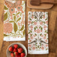 Two patterned towels on a wooden surface with a bowl of strawberries.