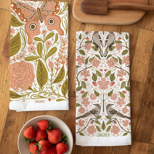 Two patterned towels on a wooden surface with a bowl of strawberries.