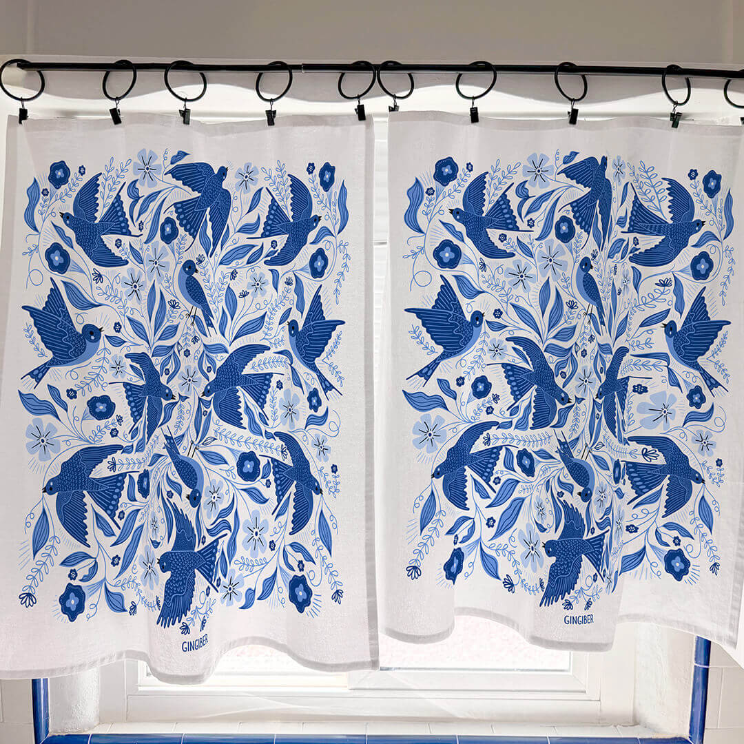 White curtains with blue bird and floral pattern hanging on a rod.