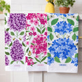 Three floral towels with purple, pink, and blue flowers displayed on a rack.