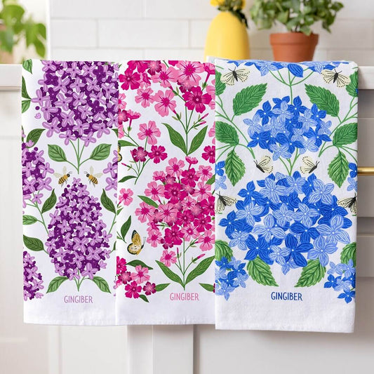 Three floral towels with purple, pink, and blue flowers displayed on a rack.