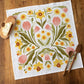 Floral patterned towel on a wooden surface with wooden spoons and a heart-shaped object.