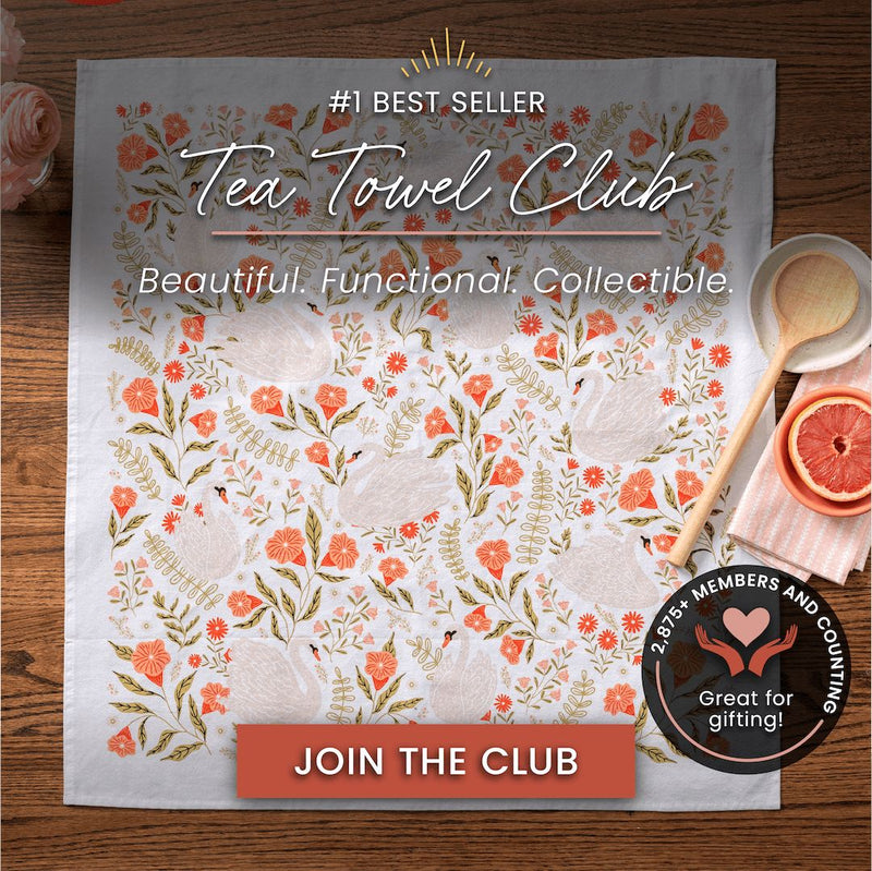 Tea towel with floral design and promotional text on a wooden surface