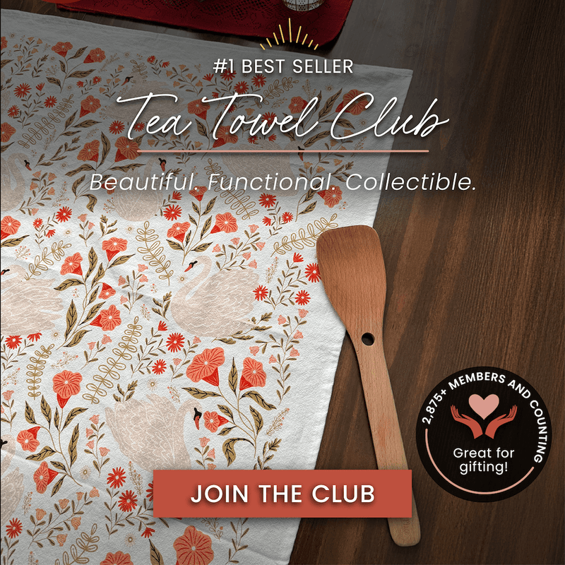 Tea towel with floral design and wooden spatula on a wooden surface, promoting the Tea Towel Club.