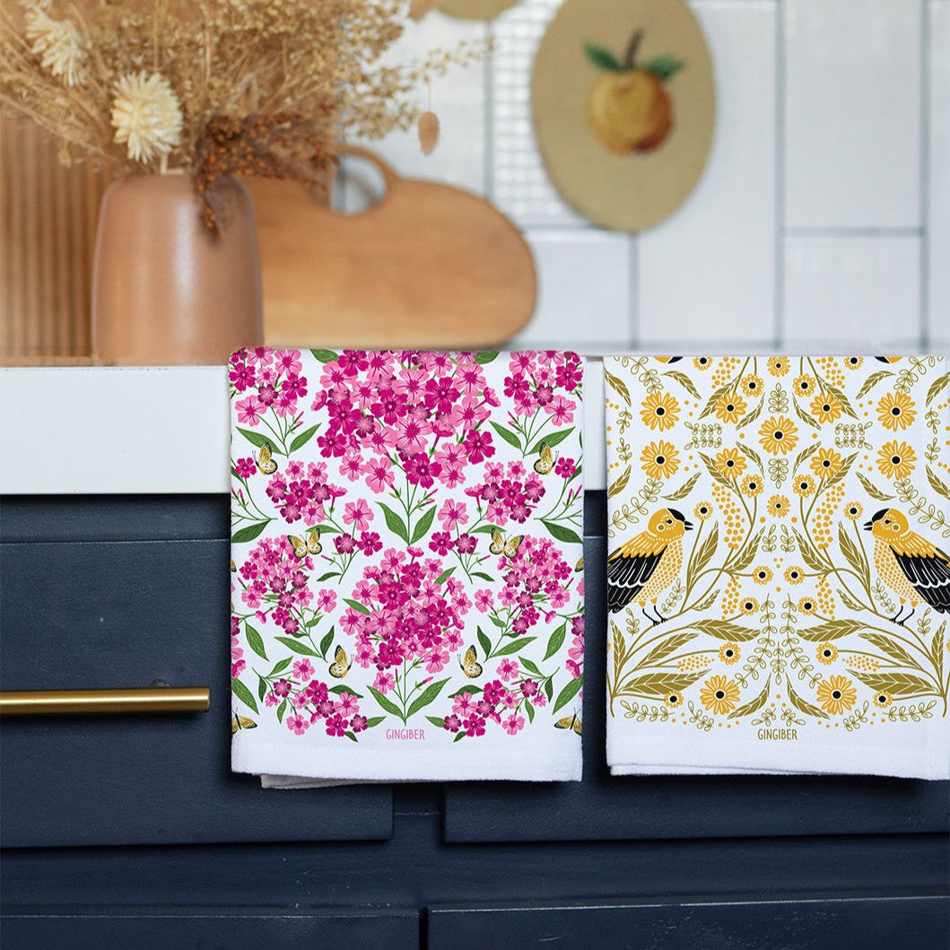 Two floral-patterned towels on a kitchen counter with decorative elements in the background.