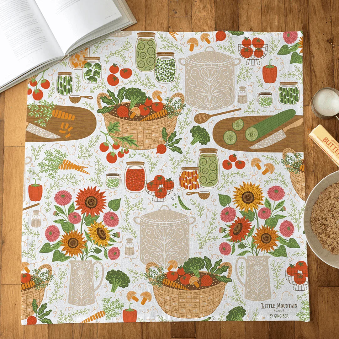 Patterned tea towel with food and floral design on a wooden surface
