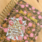 Floral daily planner with a motivational sticker on a wooden surface
